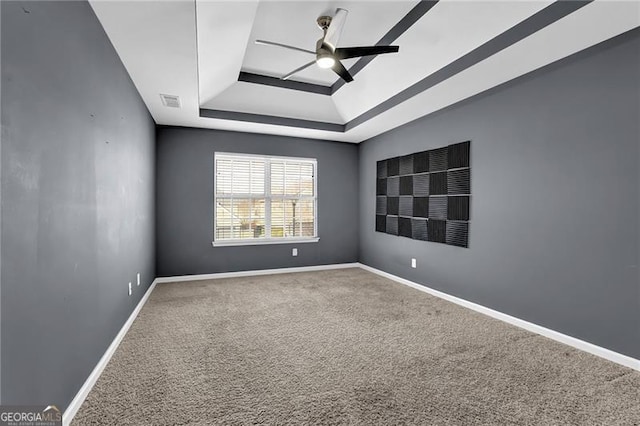 carpeted spare room featuring baseboards, visible vents, a tray ceiling, and ceiling fan