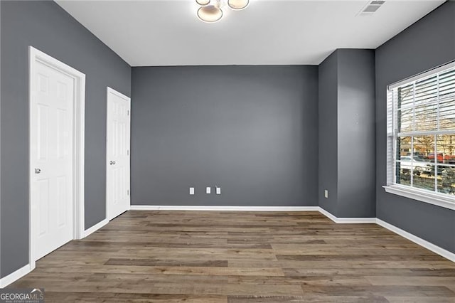 unfurnished room featuring plenty of natural light, visible vents, baseboards, and wood finished floors