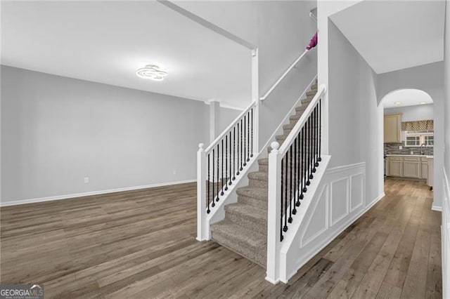 staircase featuring baseboards, arched walkways, and wood finished floors