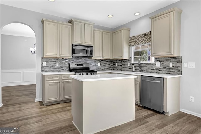 kitchen with arched walkways, appliances with stainless steel finishes, cream cabinets, light countertops, and light wood-style floors