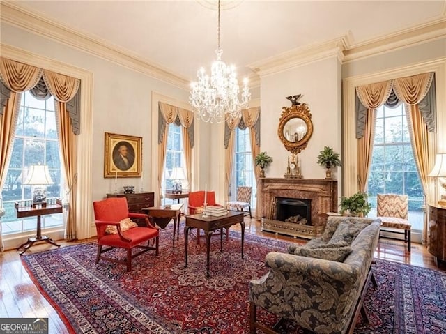 living area with wood-type flooring, a healthy amount of sunlight, a notable chandelier, and ornamental molding