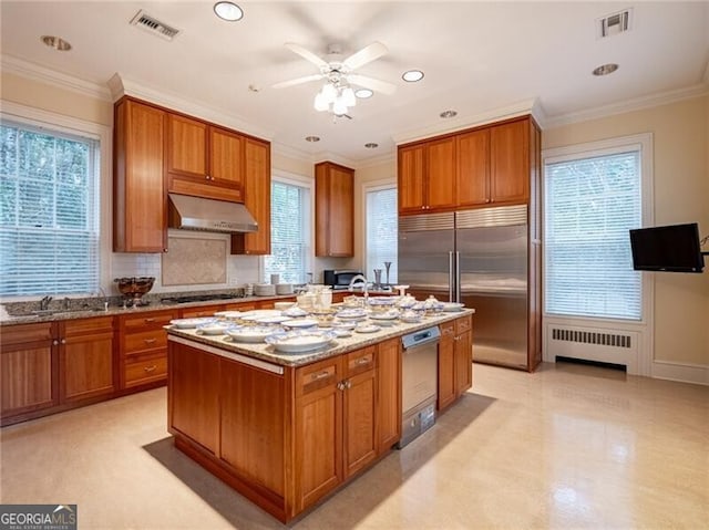 kitchen featuring radiator heating unit, stainless steel appliances, light stone countertops, and an island with sink