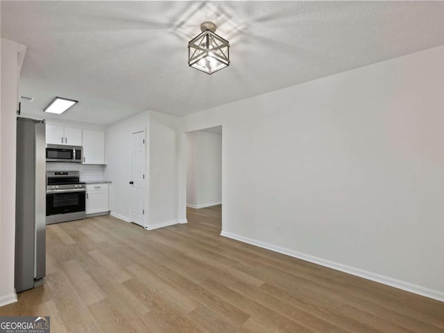 kitchen with tasteful backsplash, a textured ceiling, appliances with stainless steel finishes, light hardwood / wood-style floors, and white cabinets