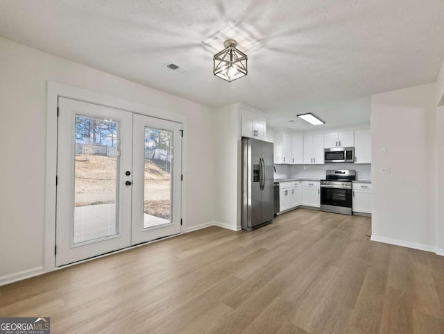 kitchen with backsplash, light hardwood / wood-style floors, white cabinets, and appliances with stainless steel finishes