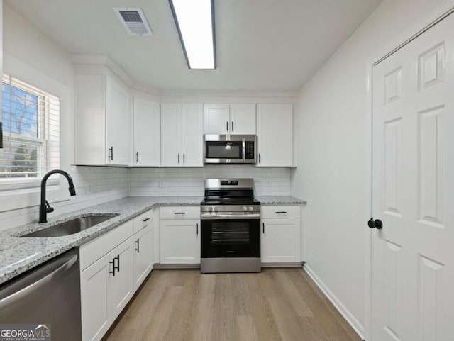 kitchen with light stone countertops, appliances with stainless steel finishes, sink, and white cabinets