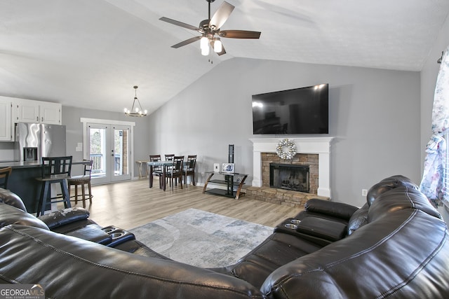 living room with french doors, vaulted ceiling, light hardwood / wood-style flooring, a fireplace, and ceiling fan with notable chandelier