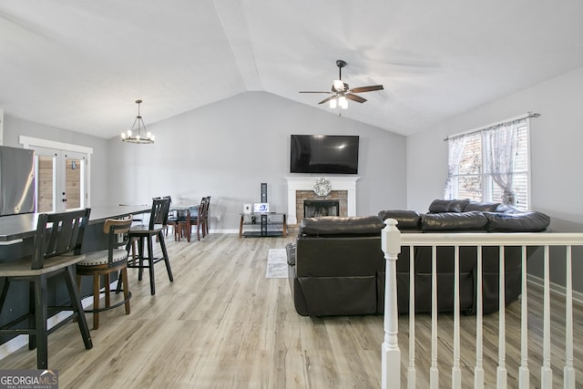 living room featuring vaulted ceiling, ceiling fan with notable chandelier, light hardwood / wood-style floors, and french doors