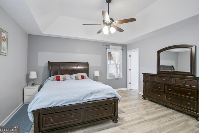 bedroom featuring ceiling fan, a raised ceiling, and light hardwood / wood-style flooring