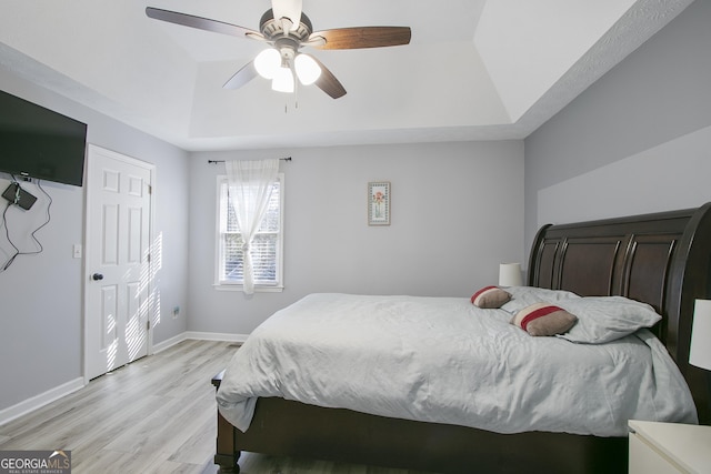 bedroom featuring ceiling fan, a tray ceiling, and light wood-type flooring