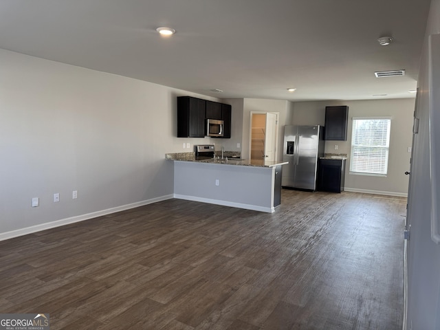 kitchen featuring sink, appliances with stainless steel finishes, light stone countertops, dark hardwood / wood-style flooring, and kitchen peninsula