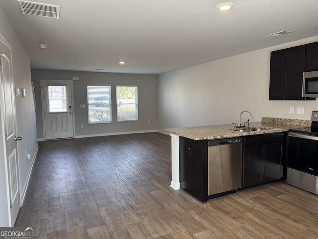 kitchen with appliances with stainless steel finishes, sink, hardwood / wood-style flooring, light stone counters, and kitchen peninsula