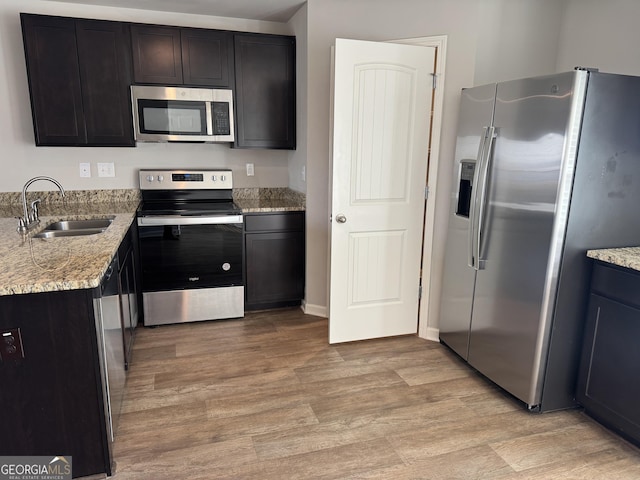 kitchen featuring appliances with stainless steel finishes, light stone countertops, sink, and light hardwood / wood-style flooring