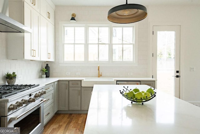 kitchen featuring appliances with stainless steel finishes, decorative light fixtures, sink, backsplash, and wall chimney range hood