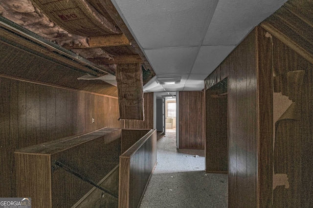 hall featuring a paneled ceiling and wooden walls