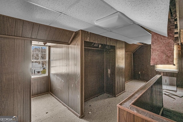 interior space with light carpet, a paneled ceiling, and wood walls