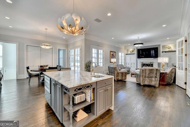 kitchen with an island with sink, light stone countertops, sink, and decorative light fixtures