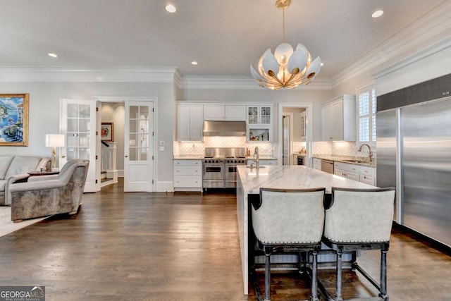 kitchen featuring white cabinetry, premium appliances, a kitchen island with sink, and hanging light fixtures