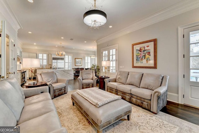 living room with crown molding, a healthy amount of sunlight, a chandelier, and light wood-type flooring