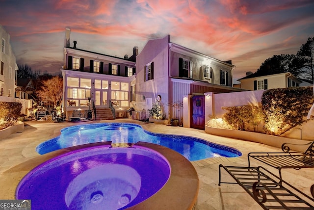 pool at dusk featuring an in ground hot tub and a patio