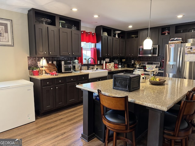 kitchen featuring a kitchen island, appliances with stainless steel finishes, sink, hanging light fixtures, and light stone counters