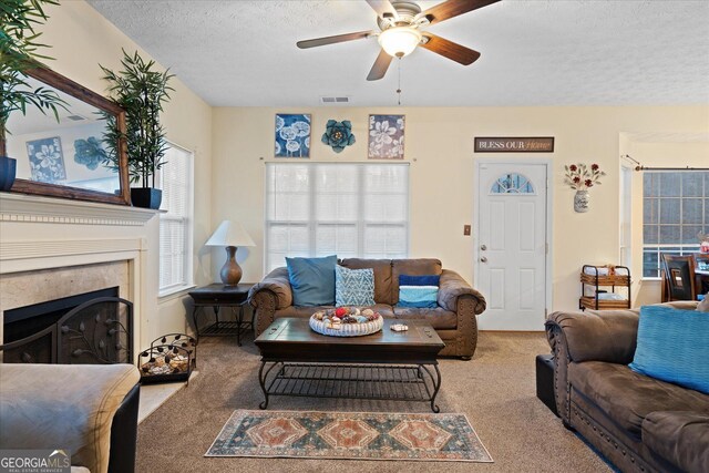 living room with light carpet, ceiling fan, a high end fireplace, and a textured ceiling