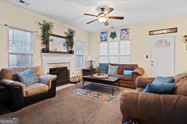 carpeted living room with ceiling fan, a high end fireplace, and a textured ceiling