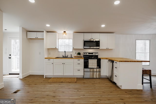 kitchen featuring butcher block countertops, sink, a breakfast bar area, appliances with stainless steel finishes, and white cabinetry