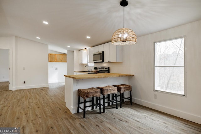 kitchen with pendant lighting, white cabinetry, a kitchen breakfast bar, kitchen peninsula, and stainless steel appliances