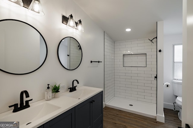 bathroom with a tile shower, vanity, hardwood / wood-style flooring, and toilet