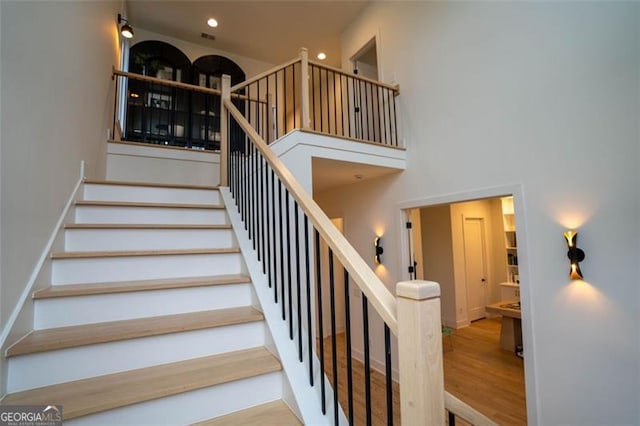 stairway featuring a towering ceiling and wood-type flooring