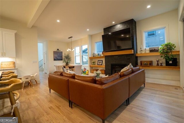 living room with a fireplace, light hardwood / wood-style floors, a chandelier, and beamed ceiling