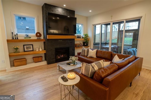 living room with a large fireplace, a wealth of natural light, and light wood-type flooring