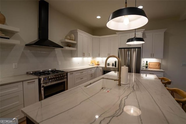 kitchen with wall chimney exhaust hood, light stone counters, hanging light fixtures, stainless steel appliances, and white cabinets