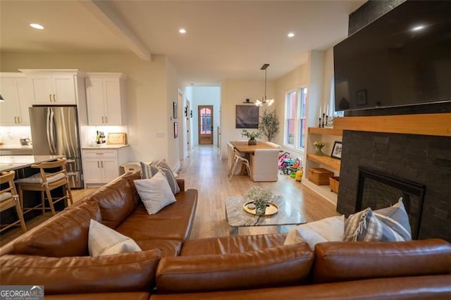 living room with light hardwood / wood-style flooring, a notable chandelier, beam ceiling, and a fireplace