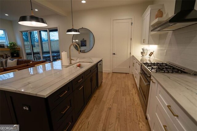 kitchen featuring wall chimney range hood, sink, appliances with stainless steel finishes, white cabinetry, and hanging light fixtures