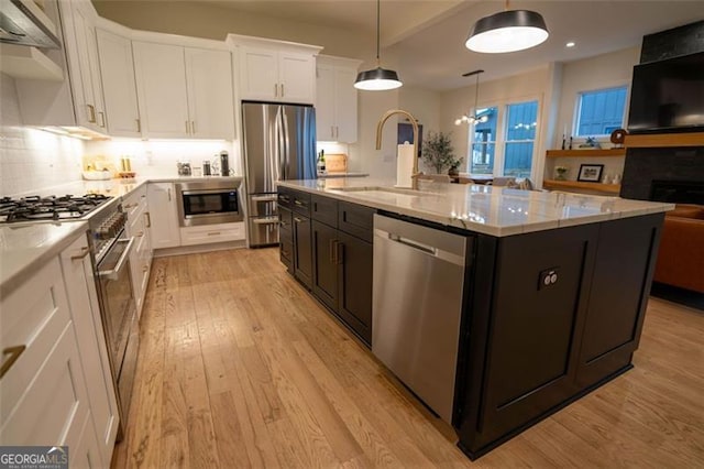 kitchen with appliances with stainless steel finishes, white cabinetry, an island with sink, sink, and hanging light fixtures