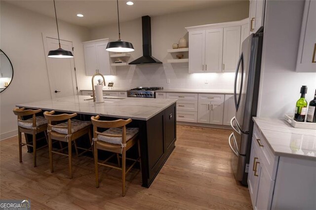 kitchen with white cabinetry, wall chimney exhaust hood, and a kitchen island with sink