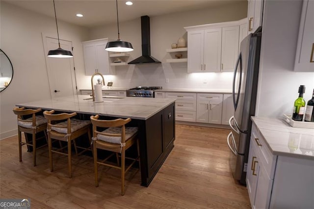 kitchen with a center island with sink, white cabinetry, and wall chimney range hood