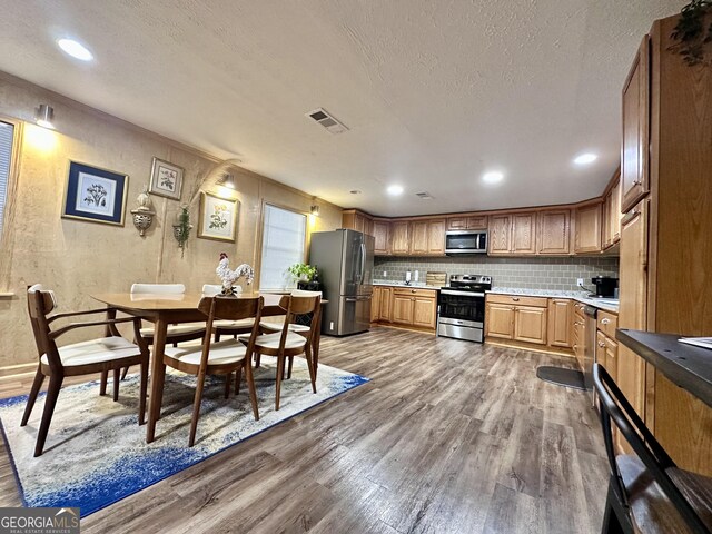 kitchen with light stone countertops, wood-type flooring, appliances with stainless steel finishes, and backsplash