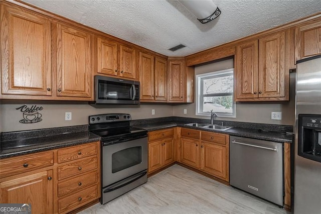 kitchen with appliances with stainless steel finishes, sink, dark stone countertops, and a textured ceiling