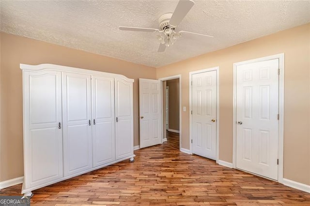 unfurnished bedroom featuring ceiling fan, two closets, a textured ceiling, and light wood-type flooring