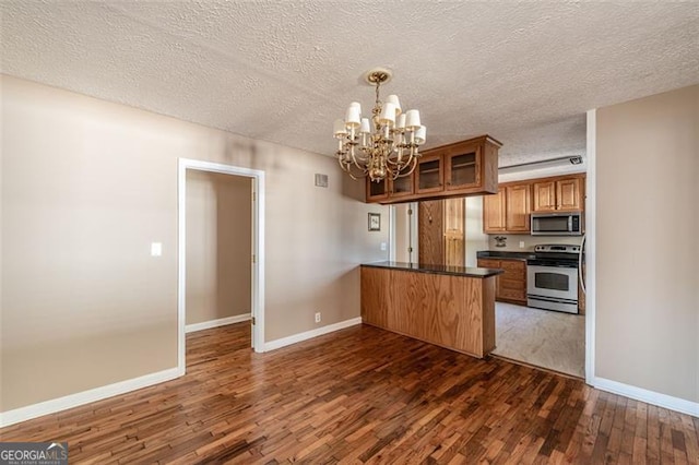 kitchen with a chandelier, hanging light fixtures, dark hardwood / wood-style flooring, kitchen peninsula, and stainless steel appliances