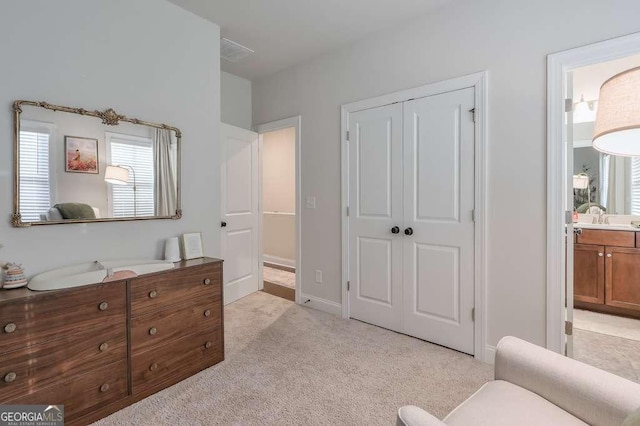 bedroom featuring light colored carpet, ensuite bathroom, sink, and a closet