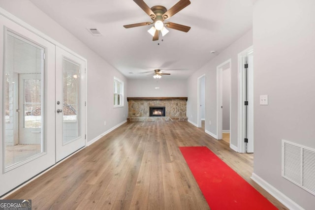 unfurnished living room with french doors, ceiling fan, a stone fireplace, and light hardwood / wood-style floors