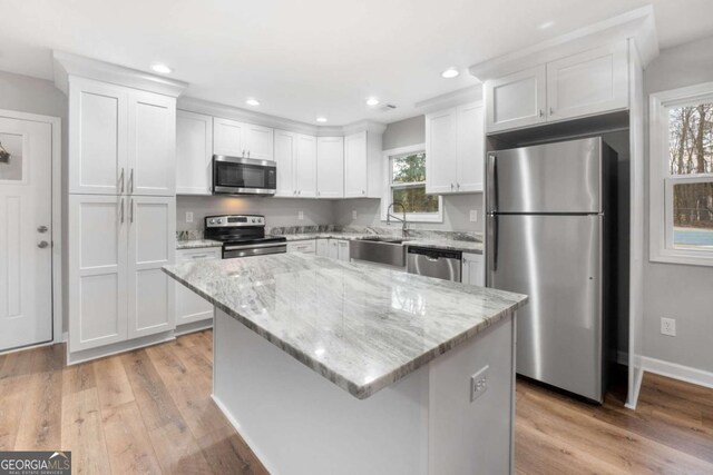 kitchen with stainless steel appliances, white cabinetry, light stone countertops, and a center island