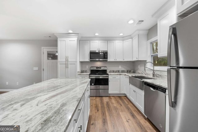 kitchen featuring stainless steel appliances, sink, white cabinets, and light stone counters