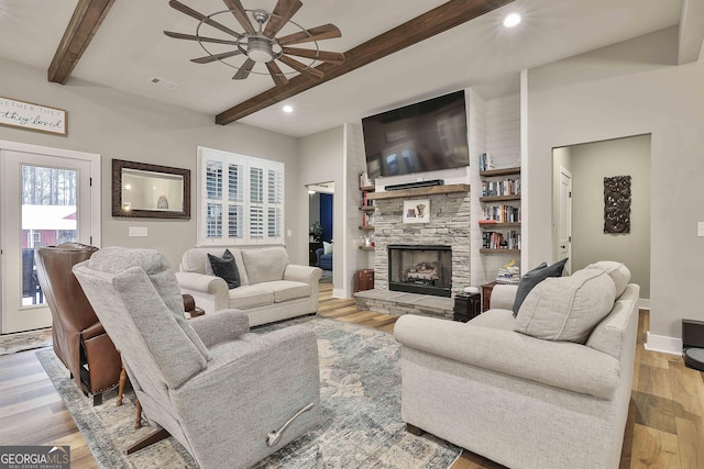 living room featuring beam ceiling, a stone fireplace, light hardwood / wood-style floors, and ceiling fan