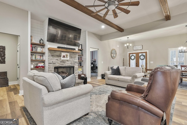 living room featuring french doors, beam ceiling, light hardwood / wood-style floors, a fireplace, and ceiling fan with notable chandelier