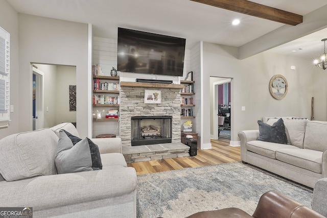 living room with beam ceiling, an inviting chandelier, a fireplace, and light wood-type flooring