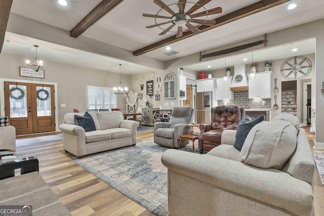 living room with beamed ceiling, ceiling fan with notable chandelier, light wood-type flooring, and french doors